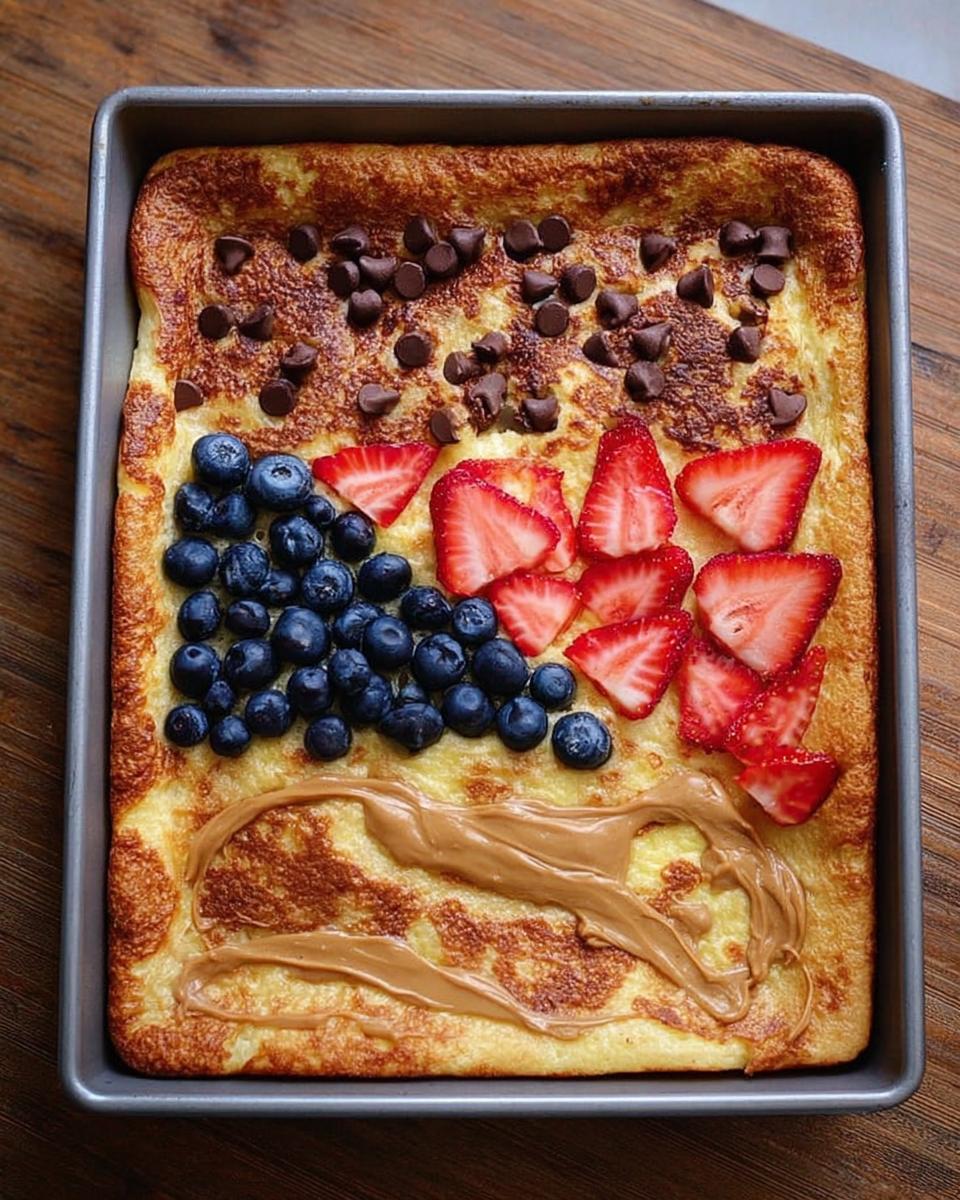 A sheet pan pancake topped with blueberries, strawberries, chocolate chips, and peanut butter, perfect for 10-Ingredient Breakfast Ideas.