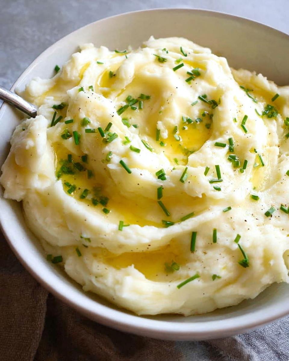 A close-up of fluffy 12-Ingredient Mashed Potatoes topped with melted butter and fresh chives.