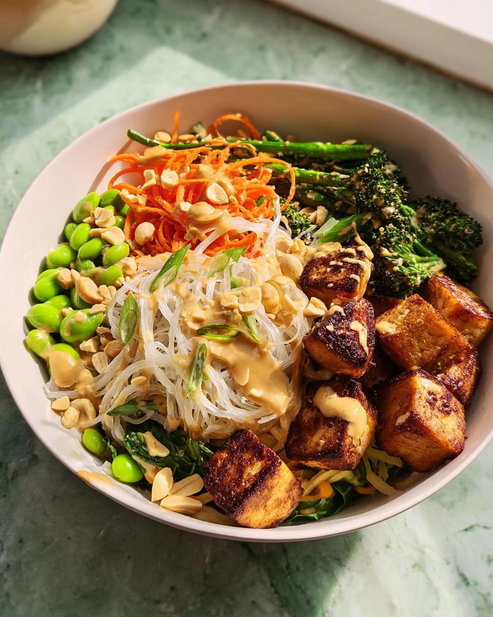 A vibrant bowl of 20-Ingredient Rice Bowl featuring crispy tofu, noodles, edamame, broccoli, and shredded carrots with peanut dressing.