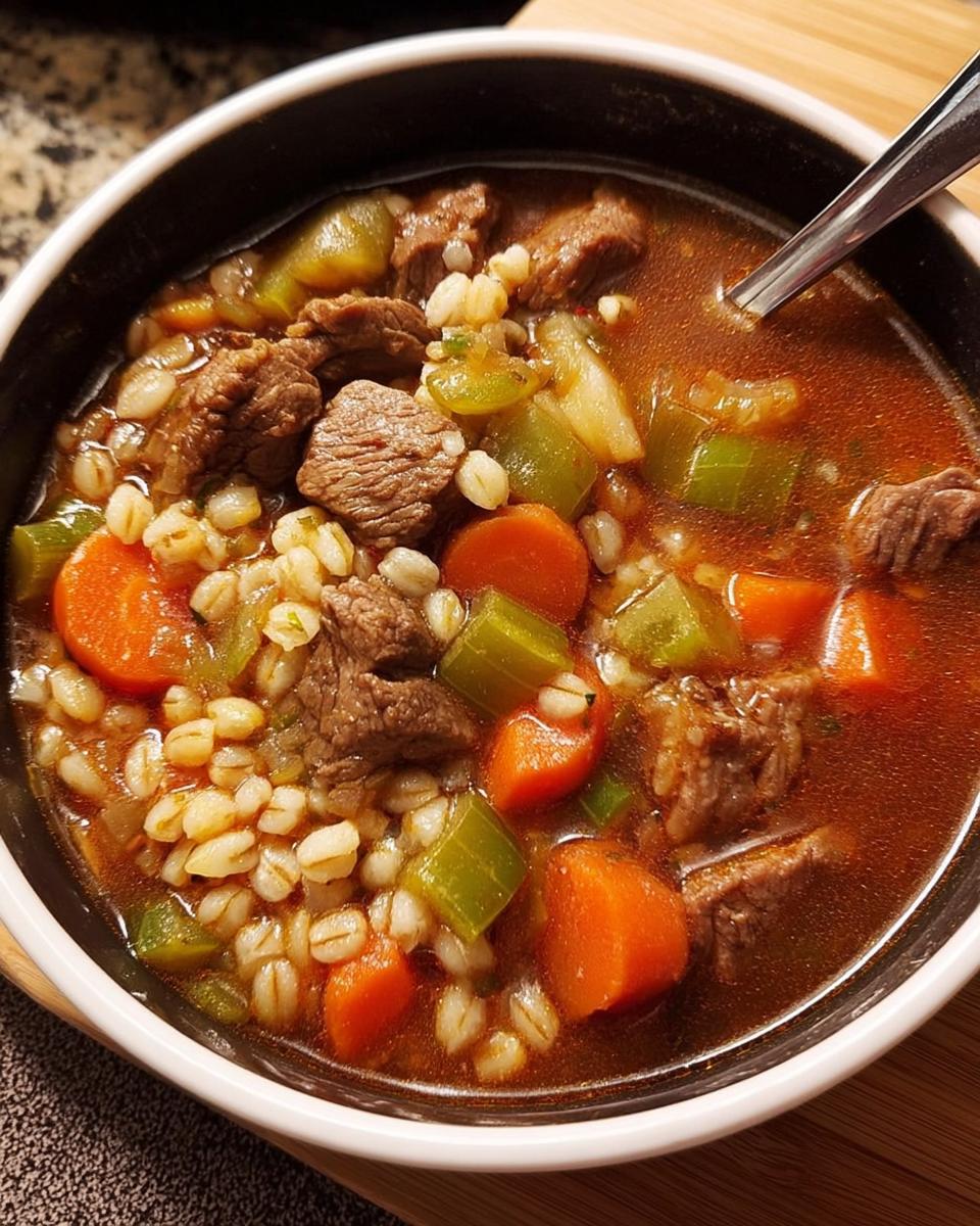 A close-up of a bowl of beef barley soup, featuring tender beef chunks, carrots, celery, and barley in a rich broth. Perfect for soup recipes meal prep.