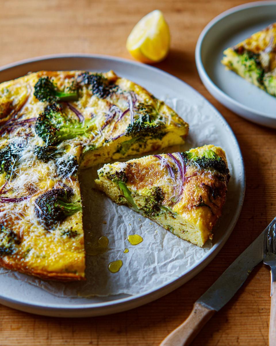 A slice of broccoli and red onion frittata, a delicious egg recipe, on a plate with a lemon wedge.