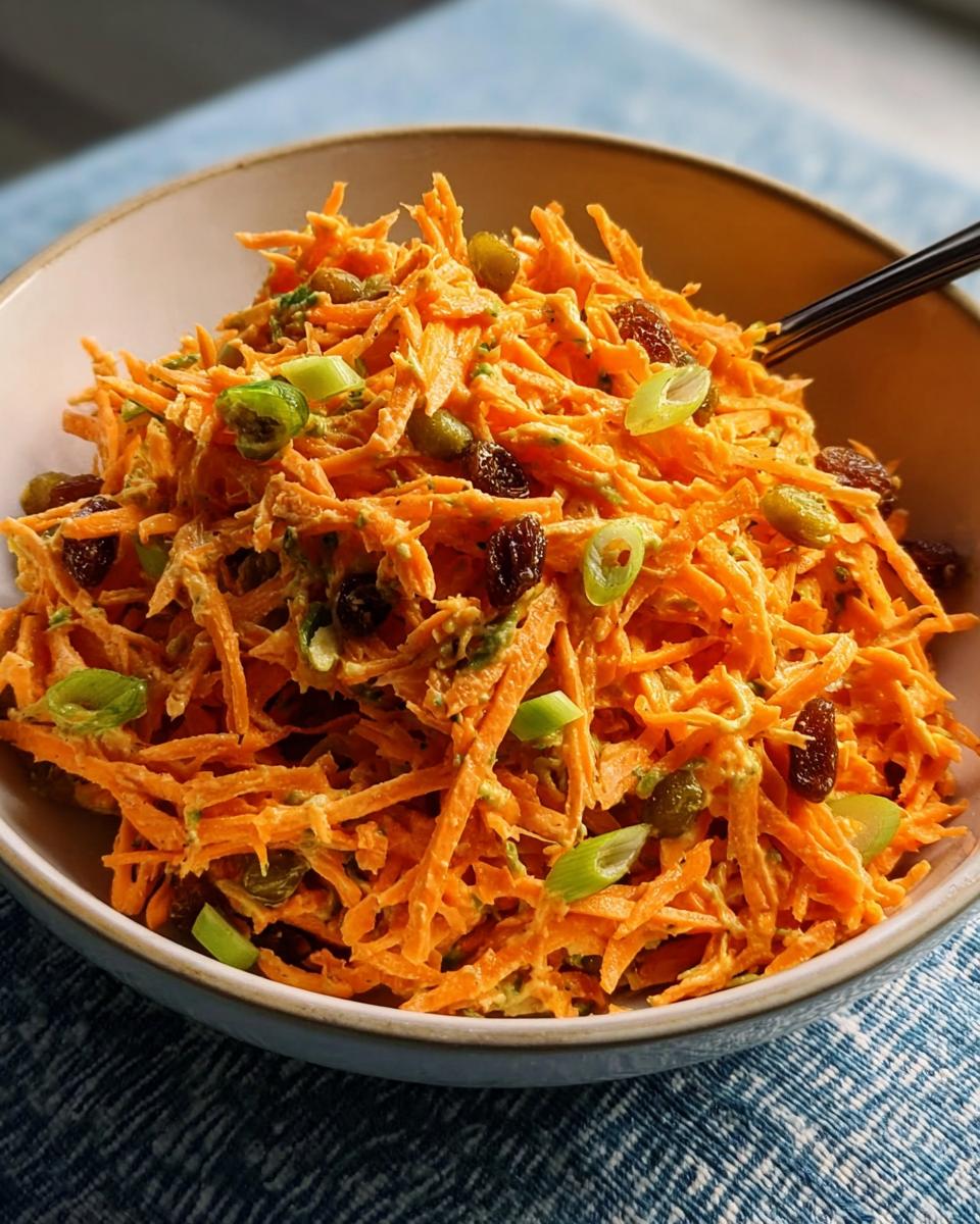 A bowl of shredded carrot salad with raisins, green onions, and a creamy dressing, perfect for quick veggie sides recipes.