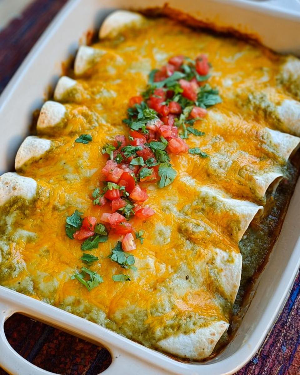 A baking dish filled with chicken enchiladas topped with green sauce, melted cheddar cheese, and pico de gallo.
