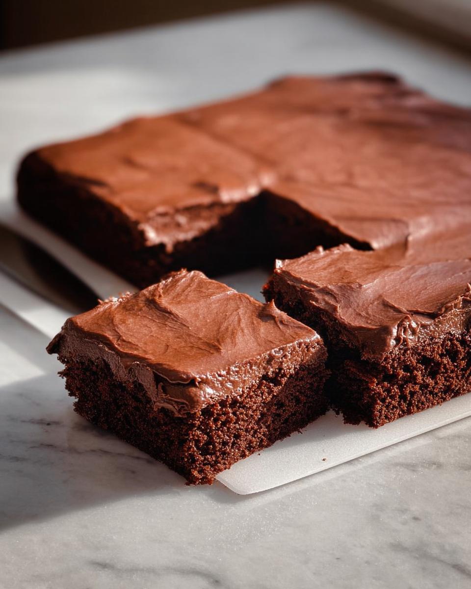 Close-up of rich chocolate cake ideas recipes, frosted with decadent chocolate frosting, cut into squares.