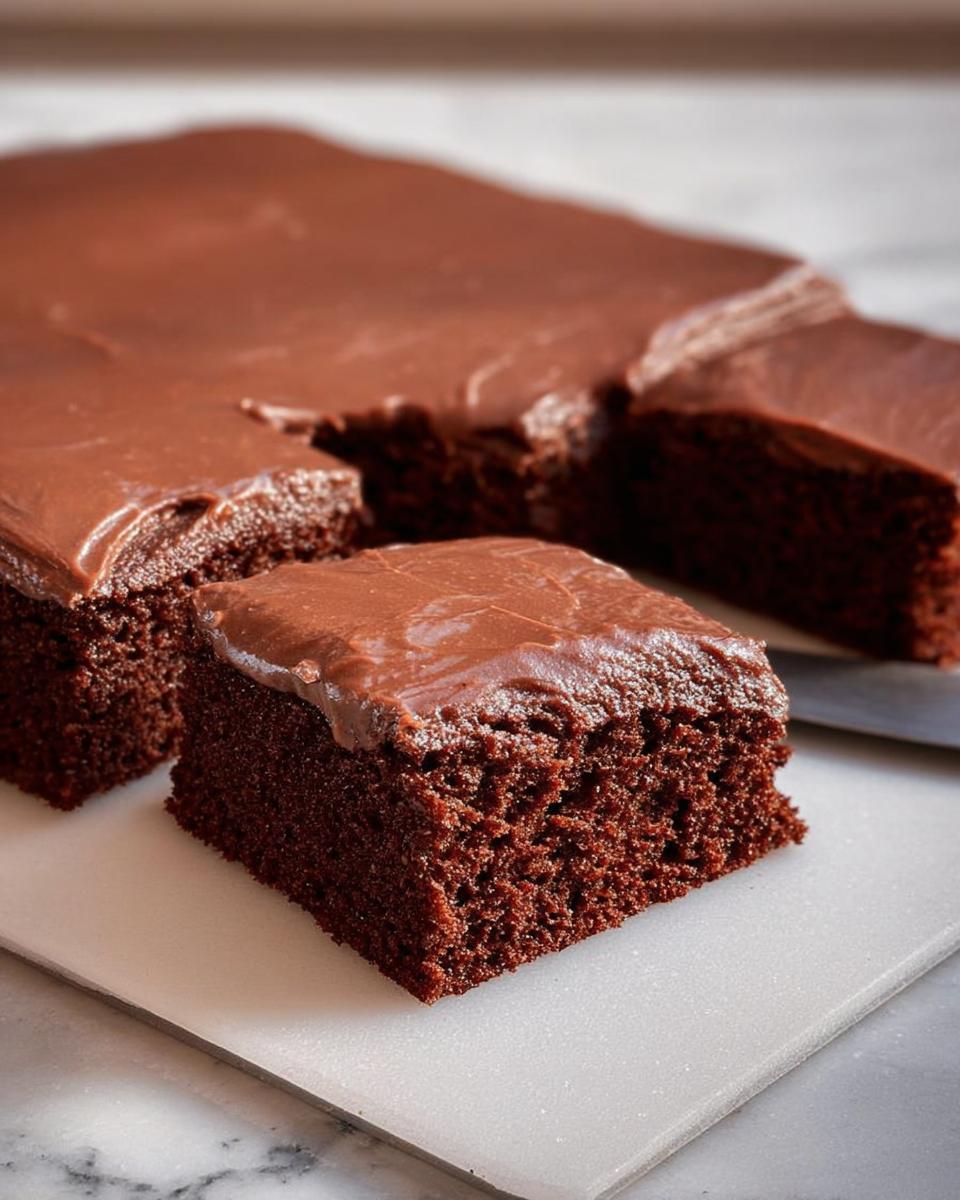 A close-up of a rich chocolate cake with smooth frosting, cut into squares, showcasing its moist texture.