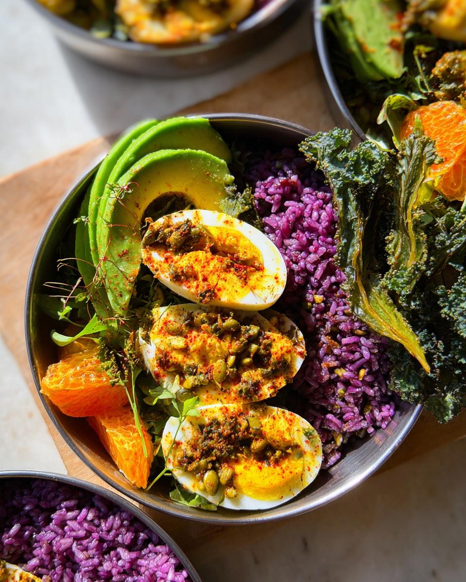 Close-up of a healthy bowl featuring halved eggs topped with spices and seeds, purple rice, sliced avocado, and orange segments.