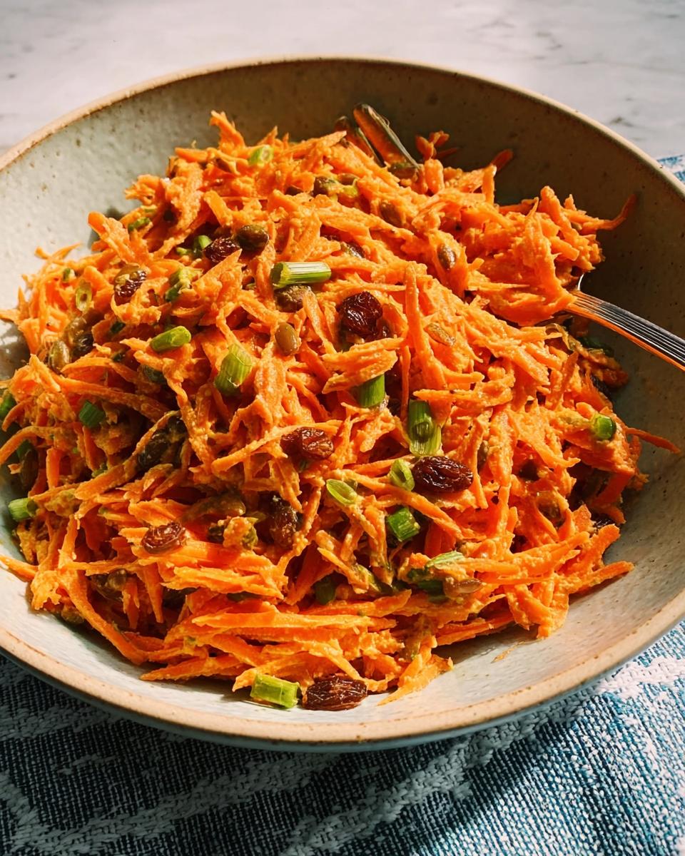 A bowl of shredded carrot salad with raisins and green onions, a perfect quick veggie side.