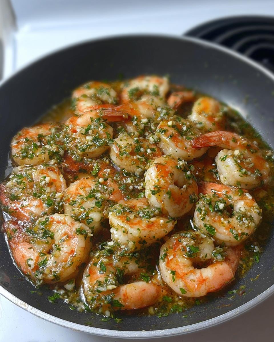 Close-up of restaurant-style garlic butter shrimp in a pan, glistening with sauce and herbs.
