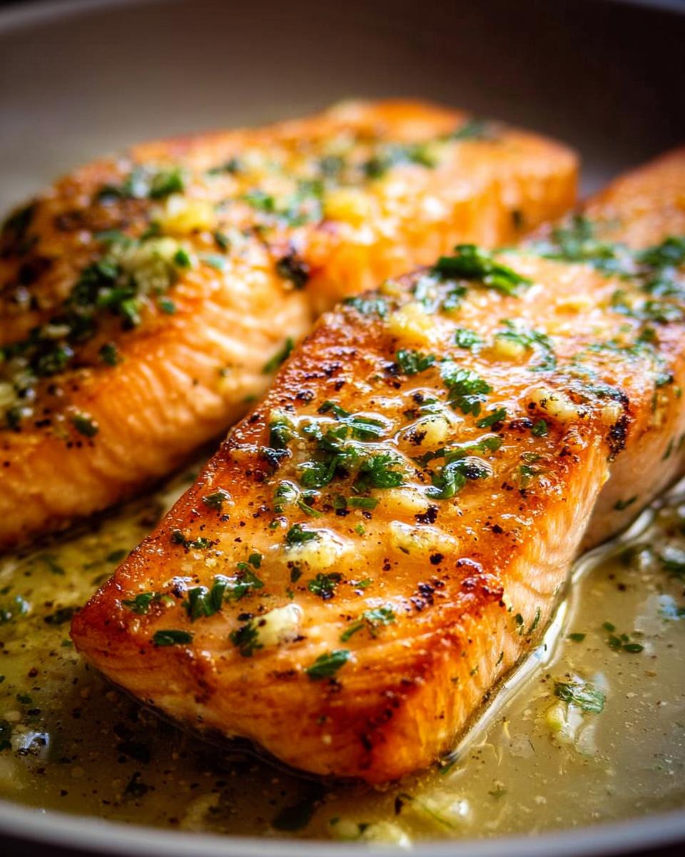 Close-up of two perfectly cooked salmon fillets, glistening with a garlic herb sauce, ready to be served.