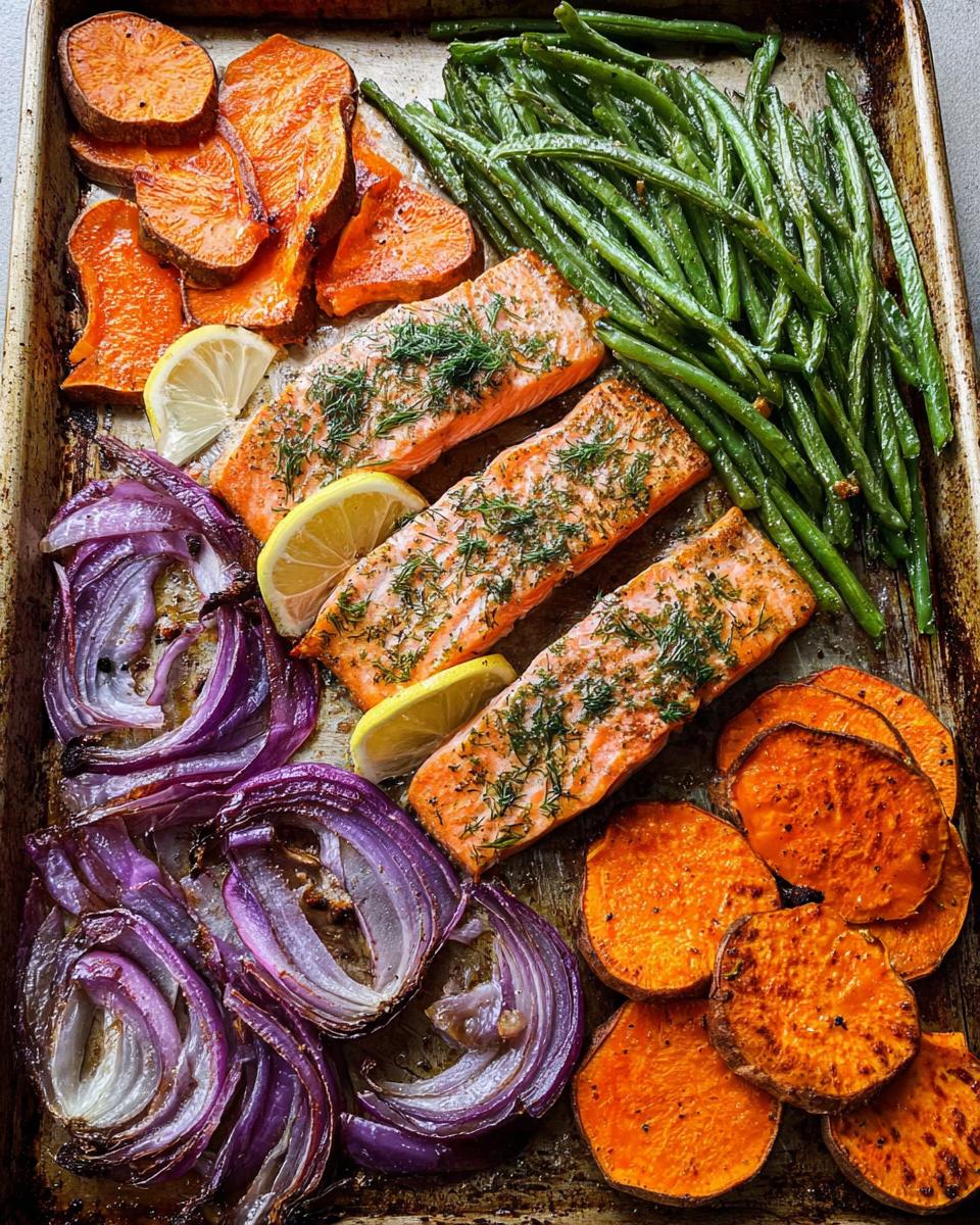 Three salmon fillets seasoned with dill, roasted sweet potato slices, red onion wedges, and green beans on a baking sheet.