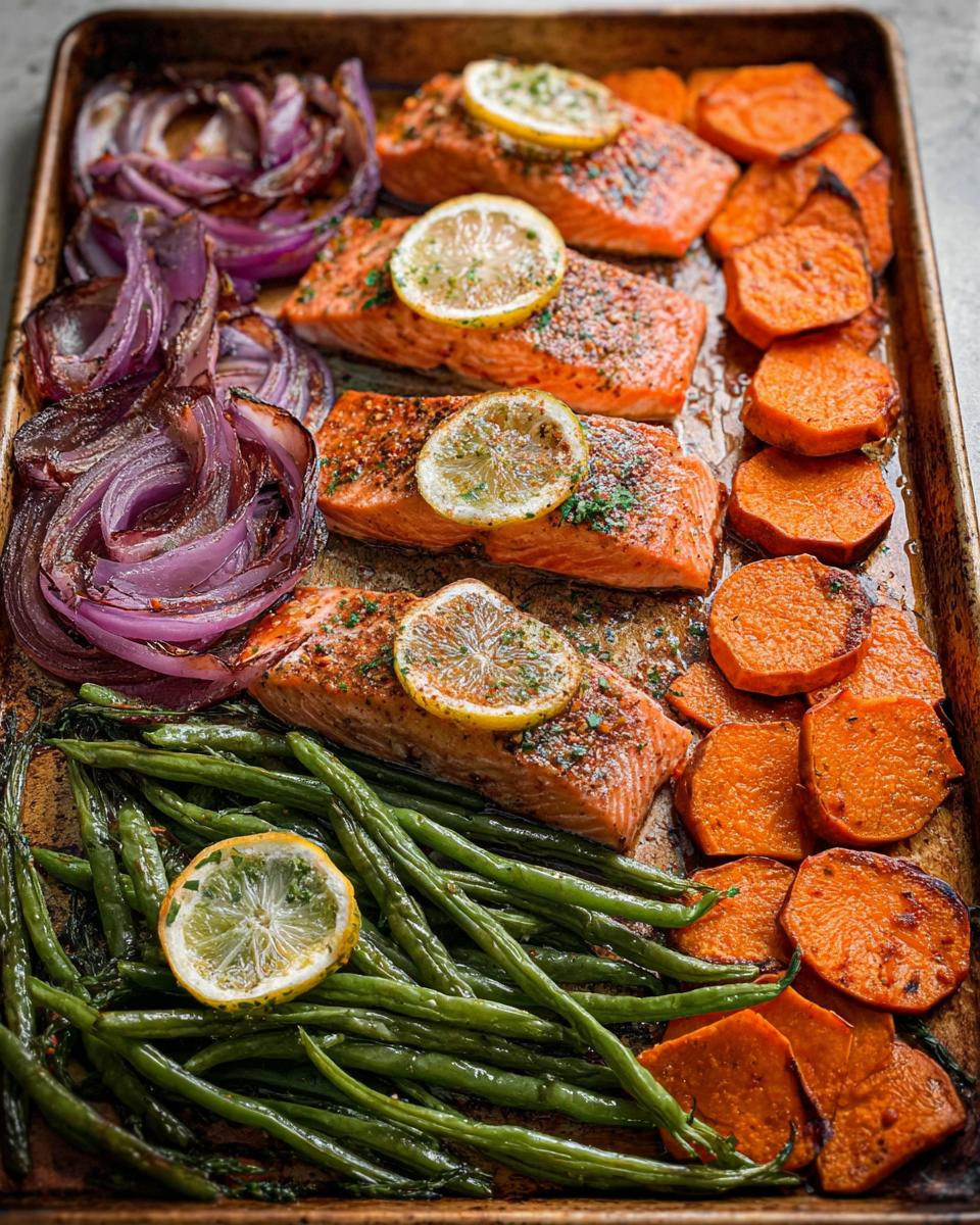 Sheet pan meal prep with roasted salmon, sweet potatoes, green beans, and red onions, garnished with lemon slices.