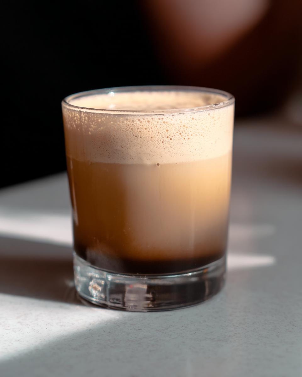 A layered Starbucks drink recipe idea with dark coffee at the bottom and creamy foam on top in a clear glass.