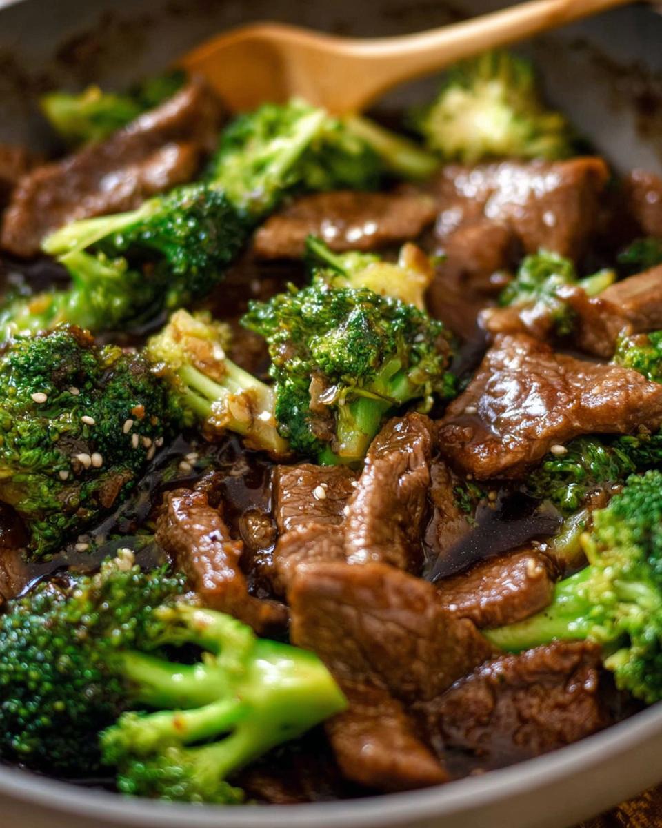 Close-up of Chinese Beef and Broccoli stir-fry in a pan with a wooden spoon.