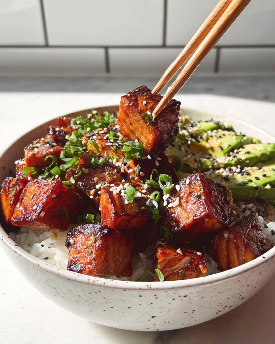 A piece of crispy salmon is lifted from a bowl of rice and avocado with chopsticks, part of a Crispy Salmon and Rice Bowl.