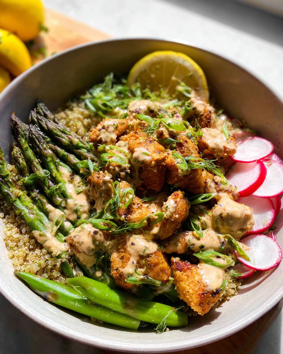 A close-up of a healthy lemon garlic chicken meal prep bowl with quinoa, asparagus, radishes, and a creamy lemon garlic sauce.