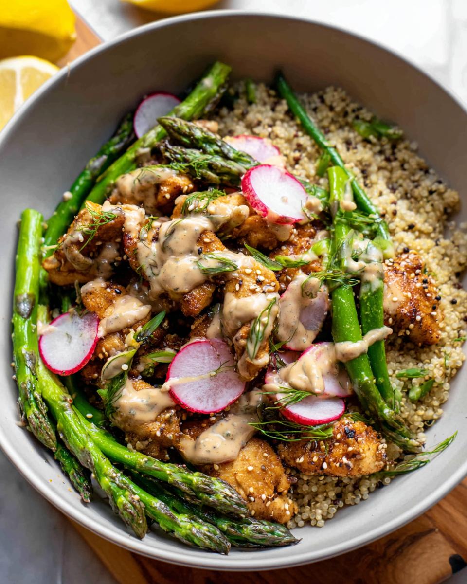 A healthy lemon garlic chicken meal prep bowl with quinoa, asparagus, radishes, and a creamy dressing.