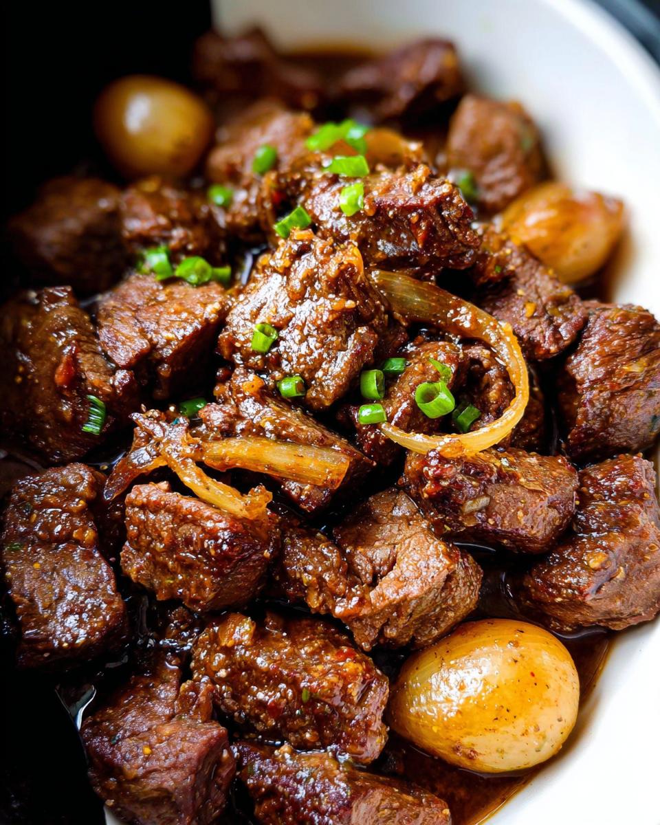Close-up of tender High Protein Slow Cooker Garlic Butter Beef Bites in a rich sauce with onions and potatoes.