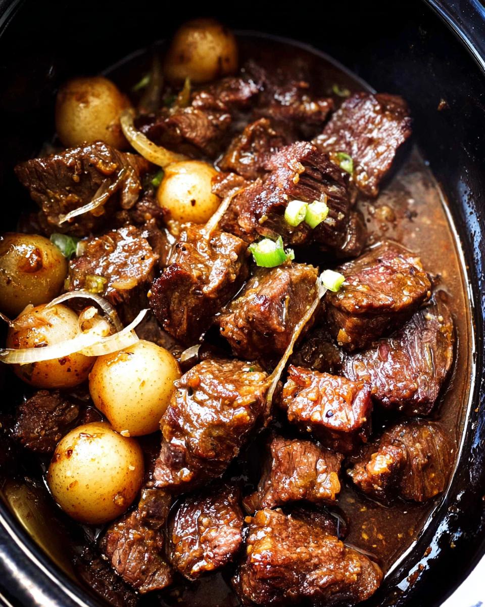 Close-up of tender High Protein Slow Cooker Garlic Butter Beef Bites with small potatoes and onions in a rich sauce.
