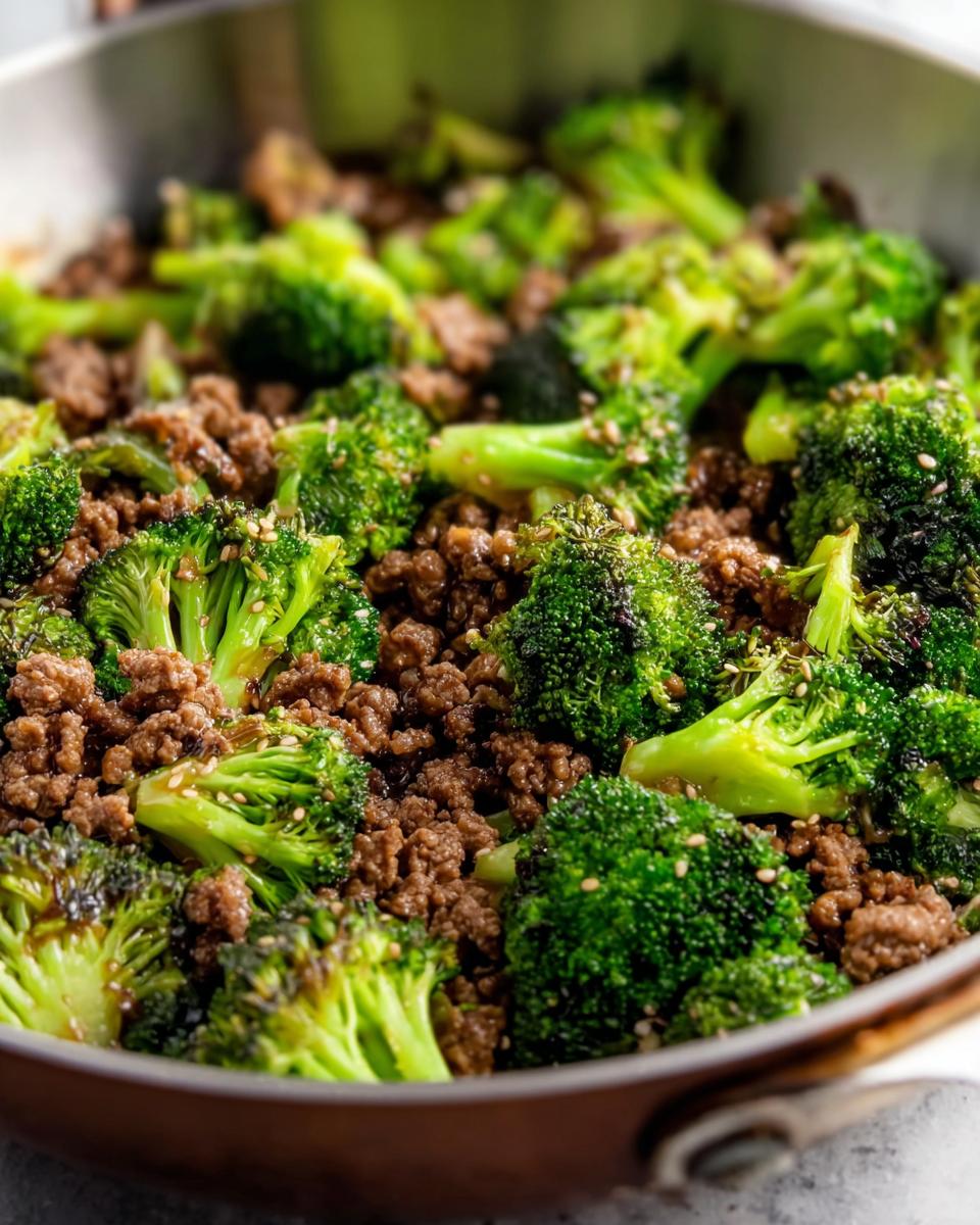 Close-up of a Keto Hamburger Broccoli Skillet in a pan, showing seasoned ground beef and bright green broccoli florets sprinkled with sesame seeds.