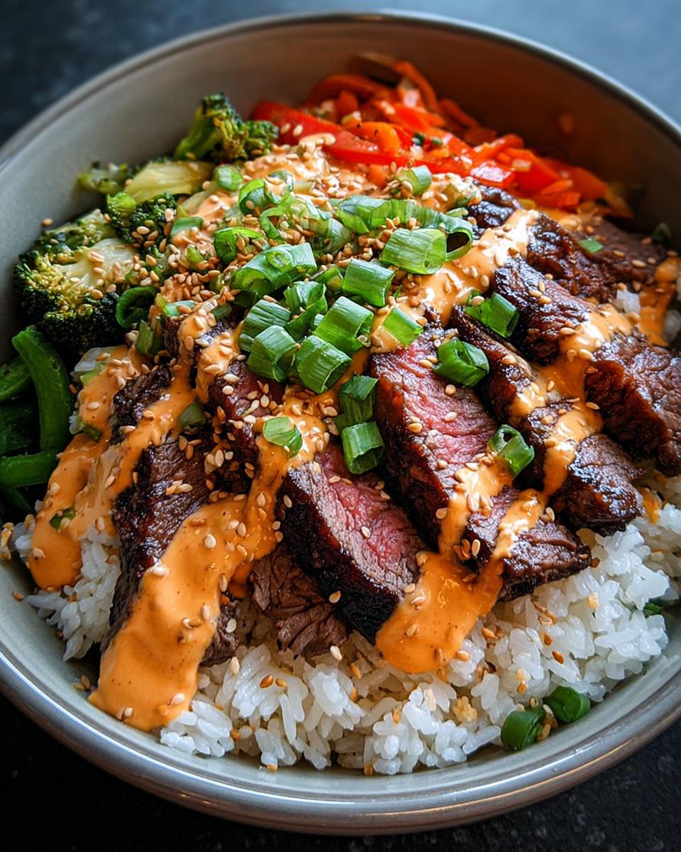 Close-up of Korean BBQ Steak Rice Bowls with sliced steak, rice, broccoli, carrots, and spicy cream sauce.