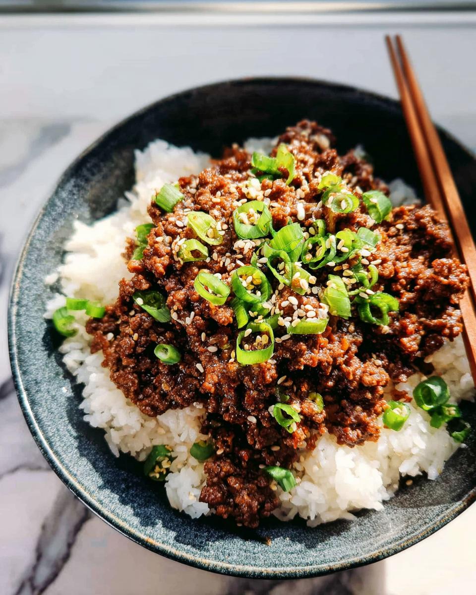 A close-up of a Korean Ground Beef Bowl served over white rice, topped with chopped scallions and sesame seeds.
