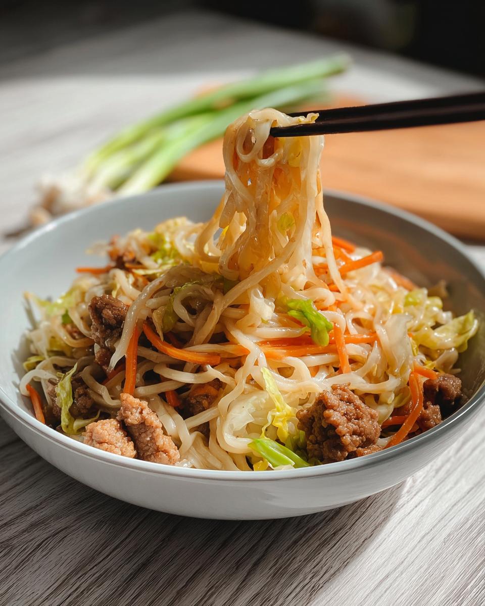 A close-up of a bowl of Potsticker Noodle Bowl with Pork & Cabbage Slaw, with noodles being lifted by chopsticks.
