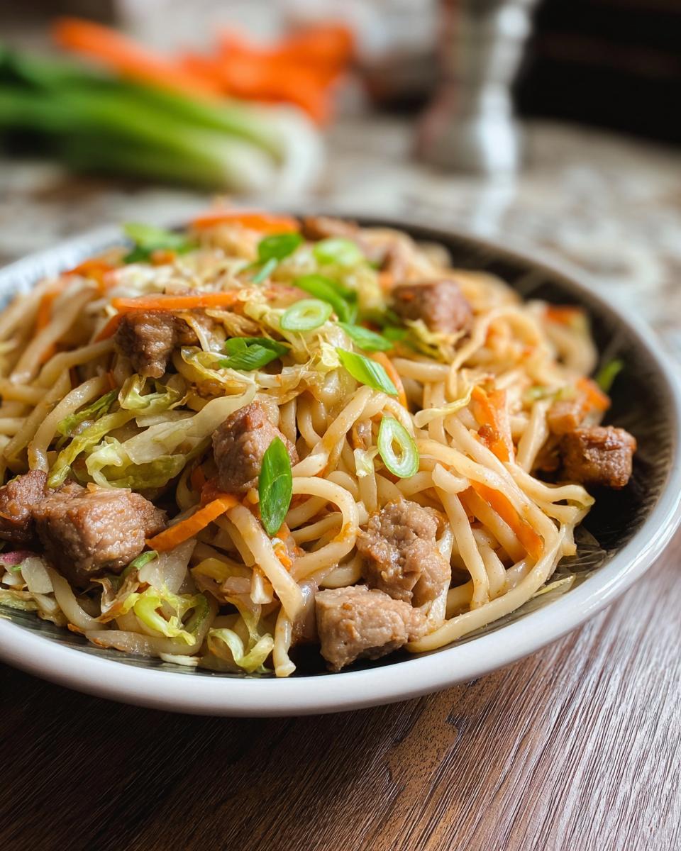 A close-up of a Potsticker Noodle Bowl with Pork & Cabbage Slaw, featuring noodles, pork pieces, shredded cabbage, and carrots, garnished with green onions.