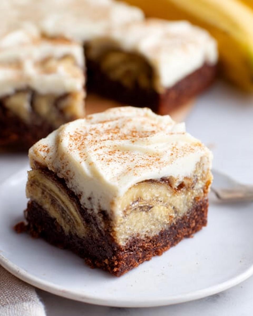 A decadent slice of Banana Bread Brownies Made Easy, featuring layers of chocolate brownie, banana slices, and creamy frosting, dusted with cinnamon.