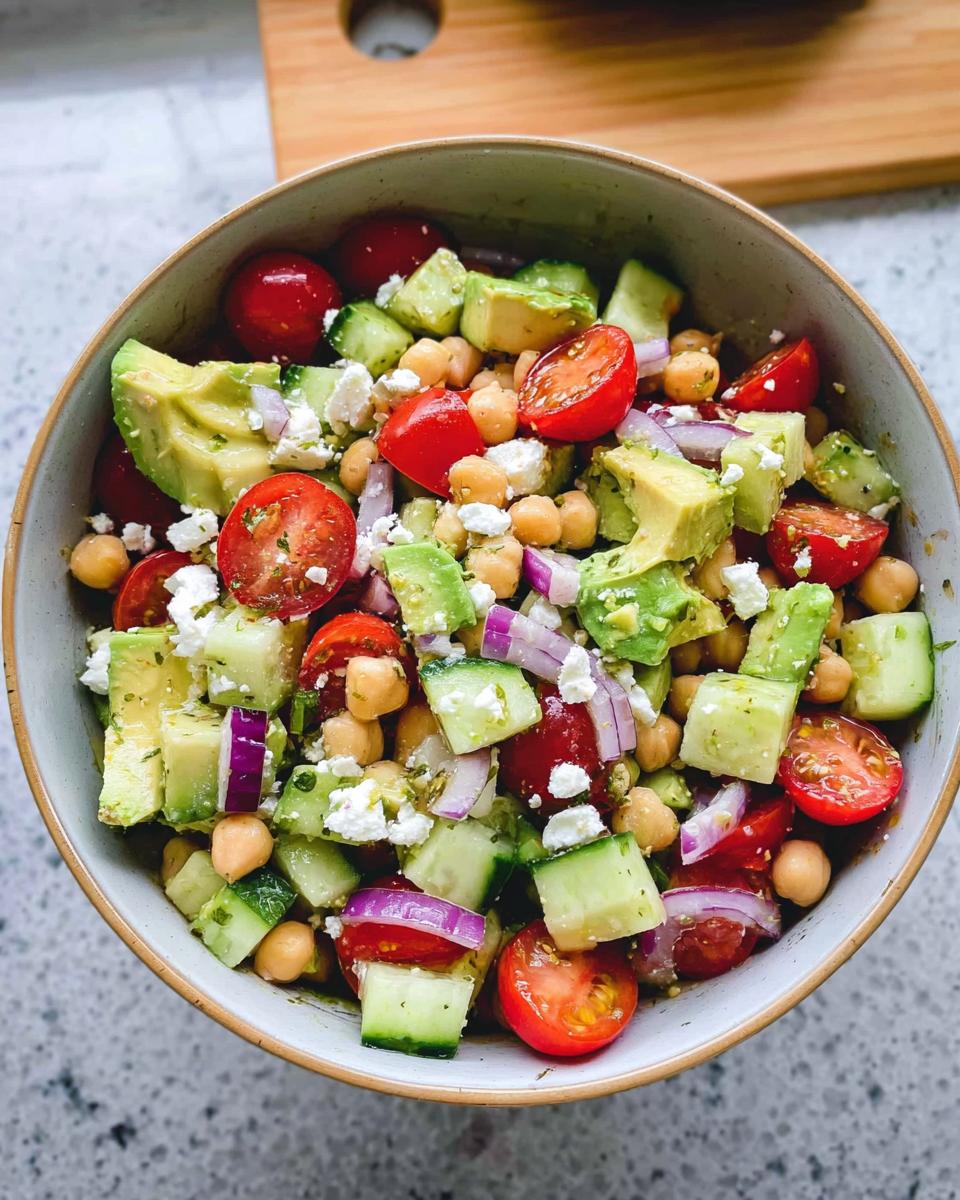 A vibrant bowl of Chickpea Feta Avocado Salad with cherry tomatoes, cucumber, red onion, and feta cheese.