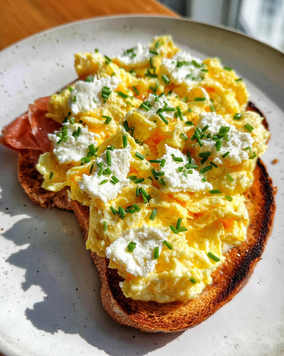 A slice of toast topped with creamy scrambled eggs, dollops of ricotta cheese, and fresh chives. This is a Creamy Ricotta Egg Toast.