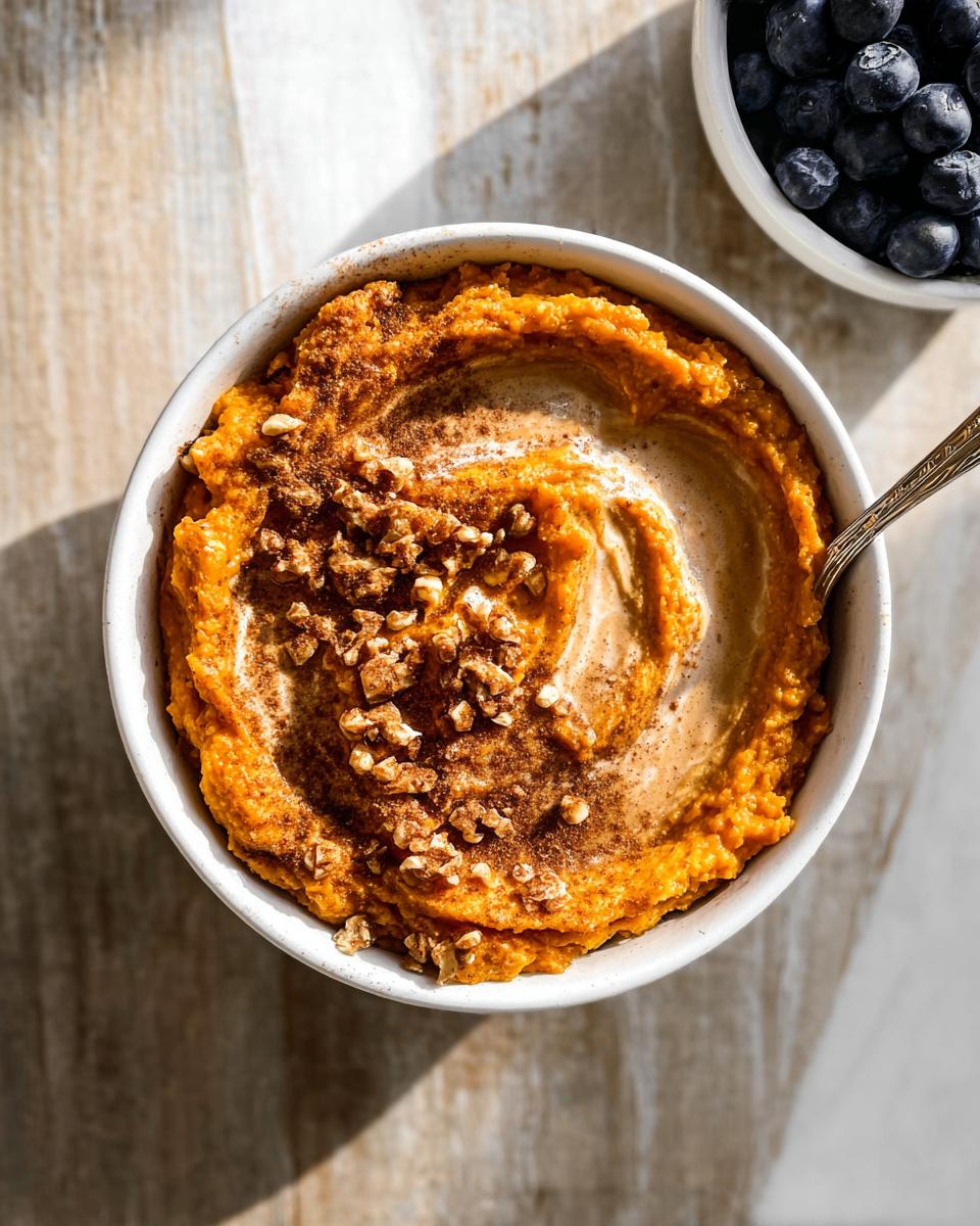 A top-down view of a Delicious Sweet Potato Breakfast Bowl topped with cinnamon and chopped nuts.
