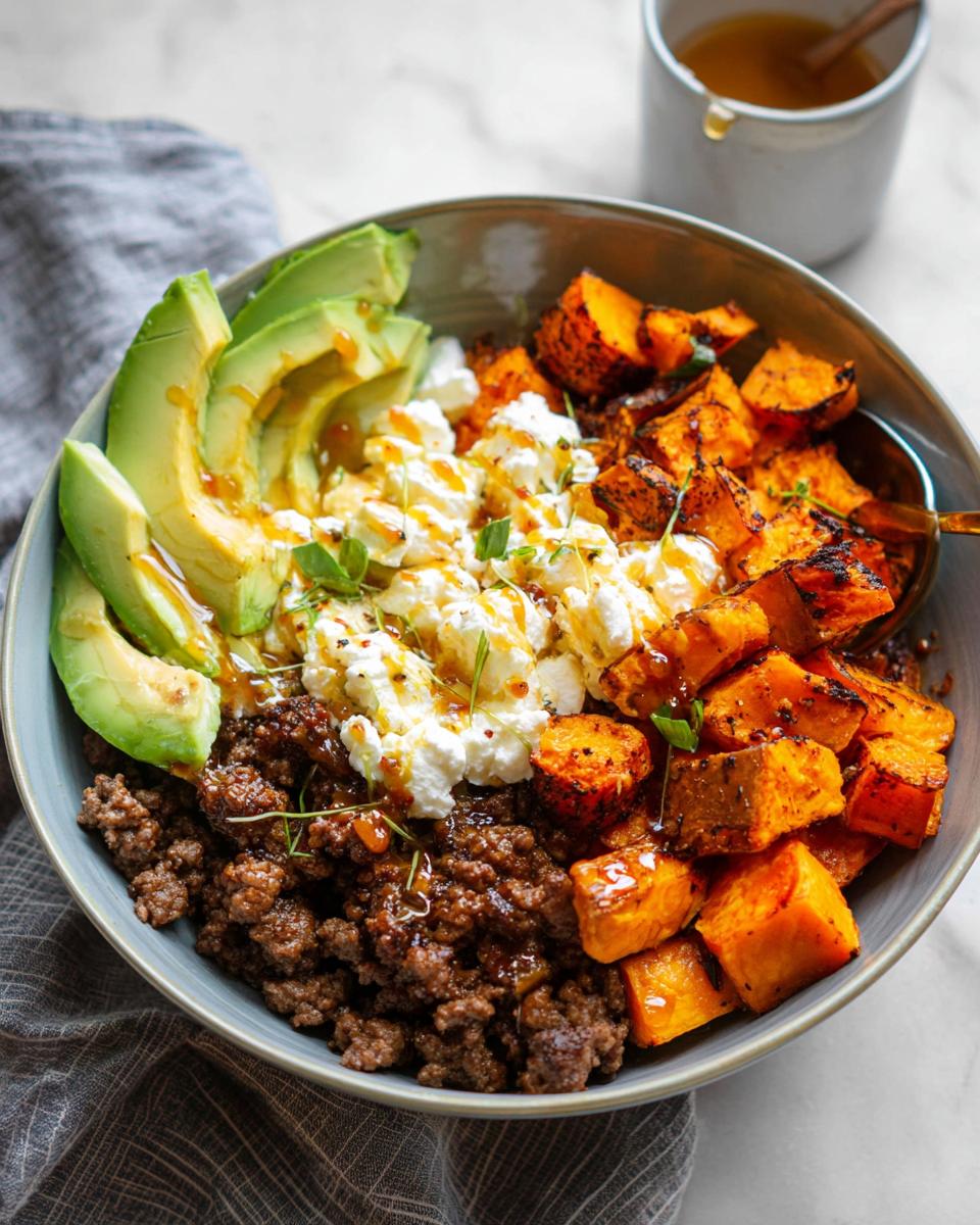 A close-up of a Ground Beef Hot Honey Bowl featuring seasoned ground beef, roasted sweet potatoes, sliced avocado, and crumbled cheese, drizzled with hot honey.