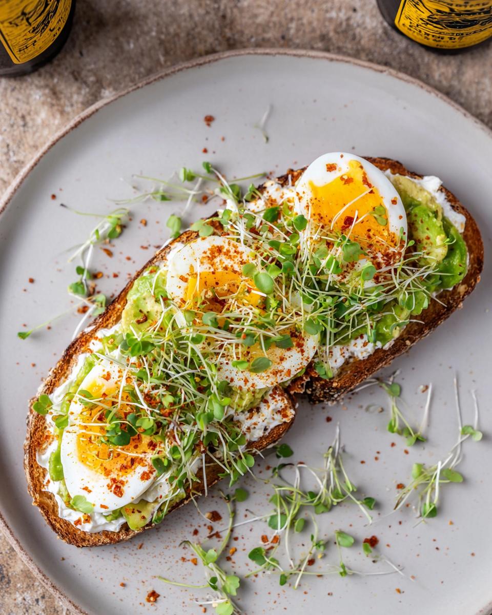 A slice of toast topped with cottage cheese, mashed avocado, sliced hard-boiled eggs, and sprouts, seasoned with chili flakes. High-Protein Breakfast Toast.
