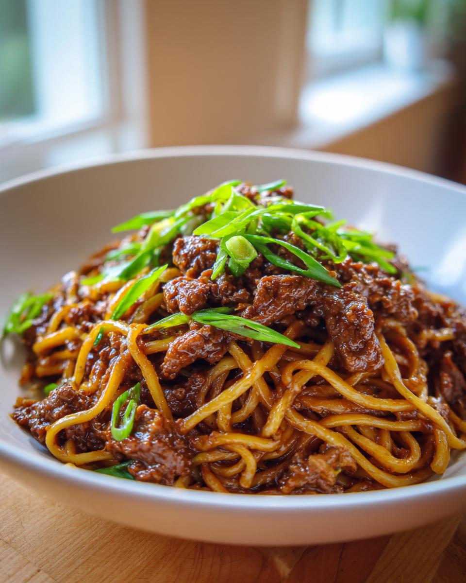A close-up shot of a bowl filled with Mongolian Ground Beef Noodles, topped with fresh green onions.