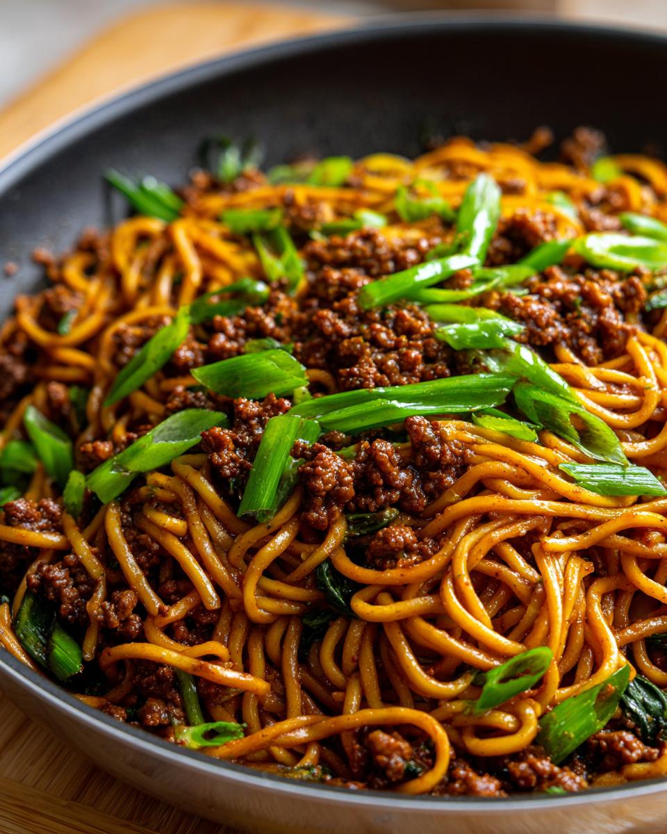 Close-up of Mongolian Ground Beef Noodles in a black pan, garnished with chopped green onions.