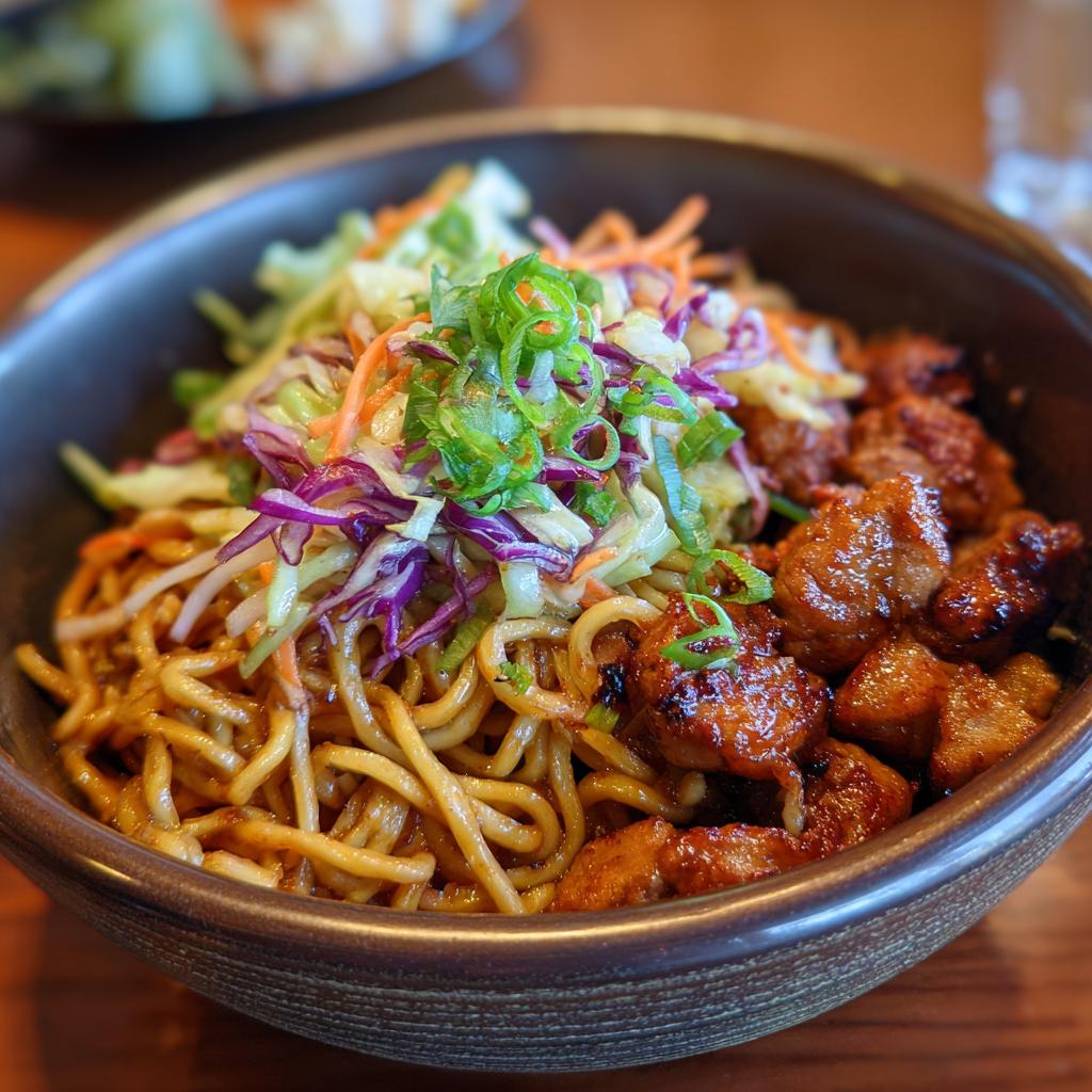 Close-up of a delicious Potsticker Noodle Bowl with tender pork pieces and a vibrant cabbage slaw topping.
